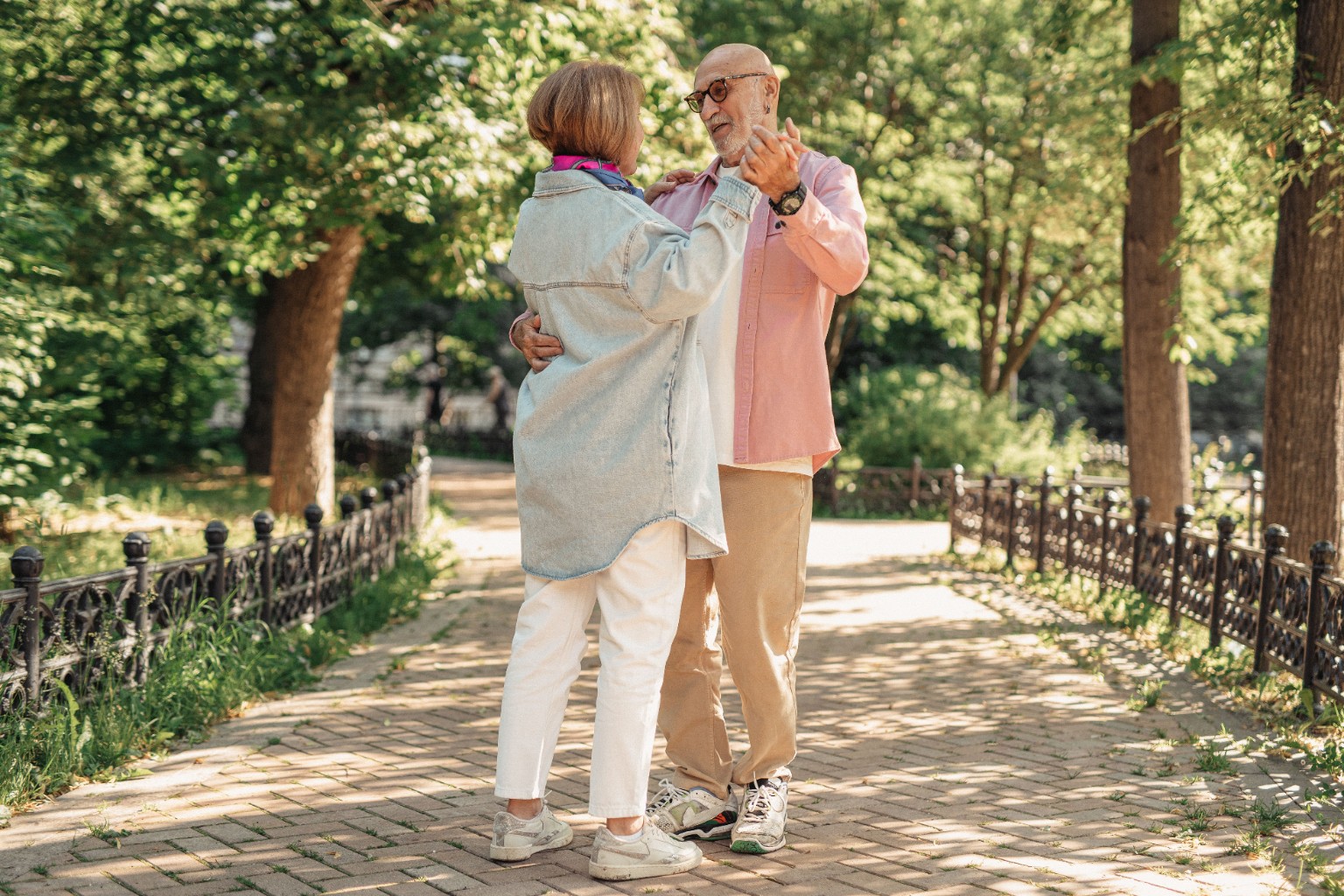 An older couple dancing together on a tree-lined path
