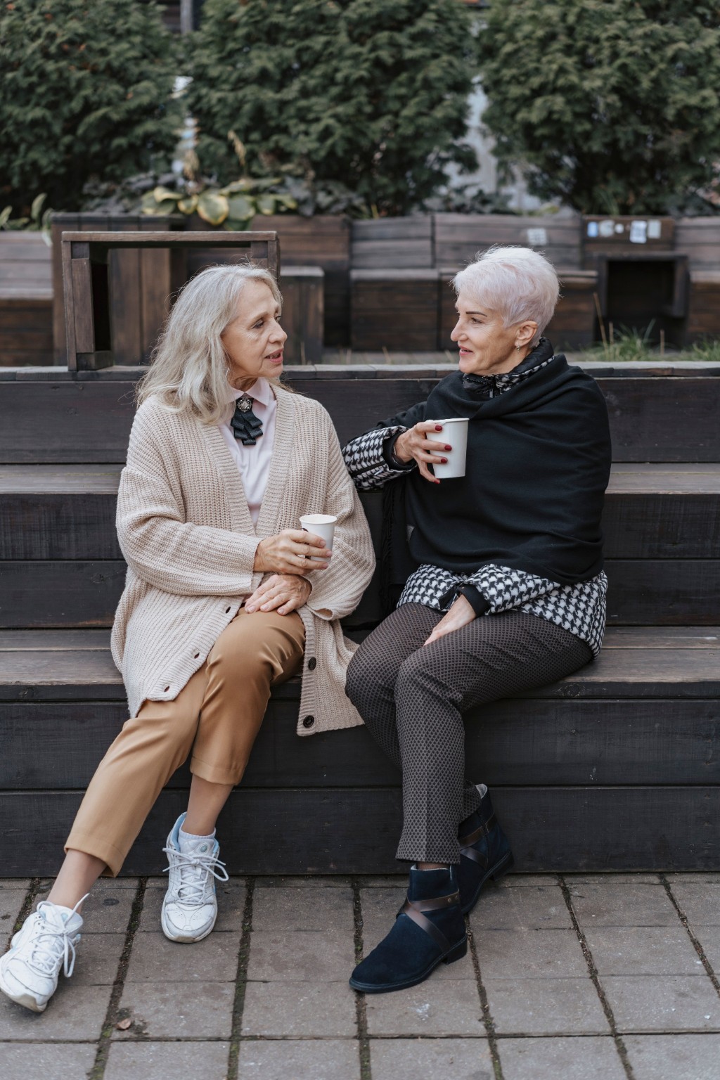 Two older women talking over coffee on a bench